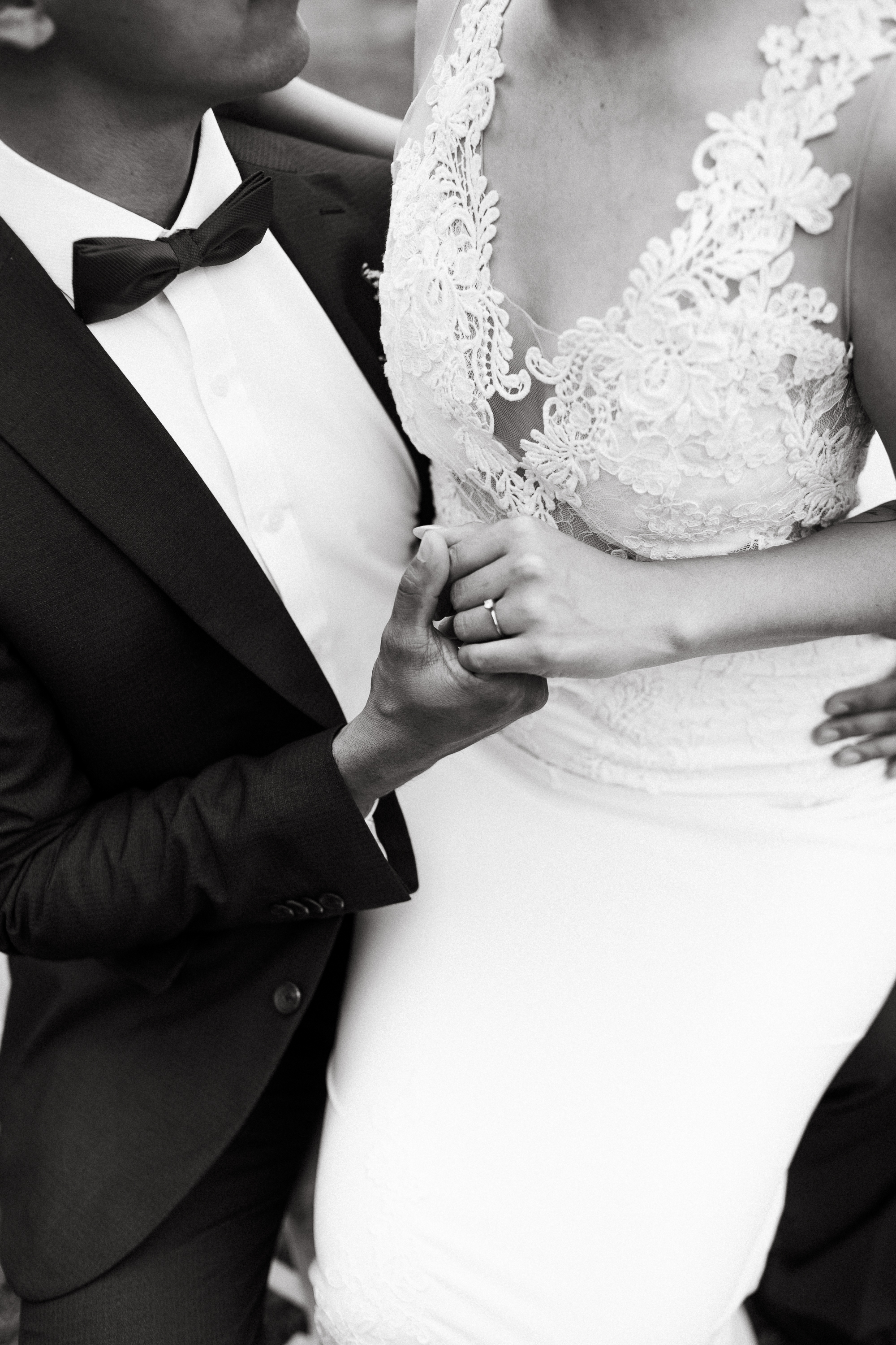 Black and white wedding photo — the bride in a mermaid gown sits on the groom's lap in a blue tuxedo, his hand tenderly holding hers as her engagement ring shows; an intimate moment by David Tovar, destination wedding photographer in Mexico